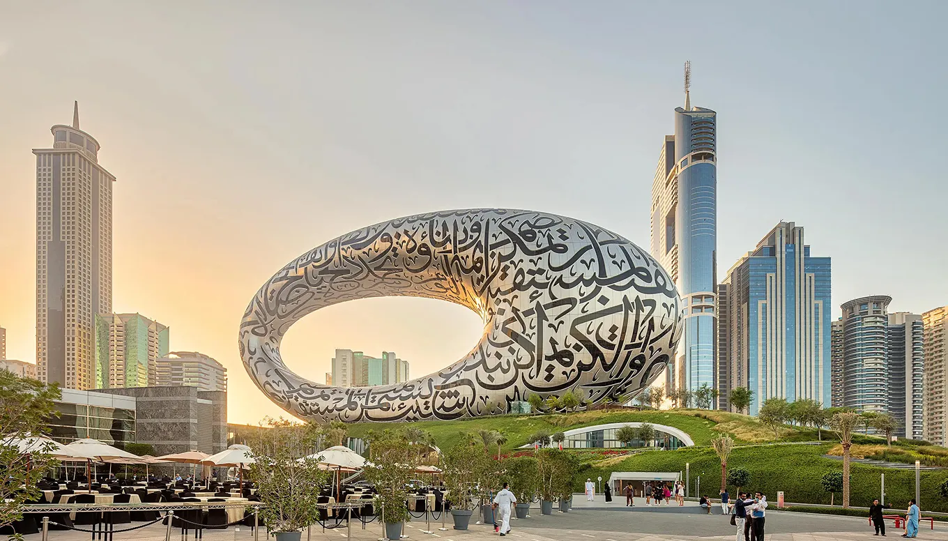 The Museum of the Future in Dubai with Arabic calligraphy on its torus-shaped structure, surrounded by modern skyscrapers and people walking nearby.