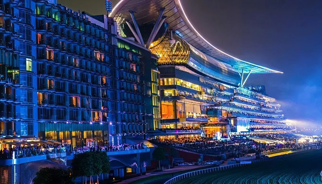 Illuminated modern grandstand at a racetrack at night with crowds of spectators.