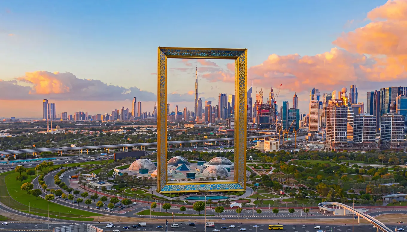 Dubai skyline at sunset with a large golden Dubai Frame structure in the foreground and the Burj Khalifa centered inside the frame.