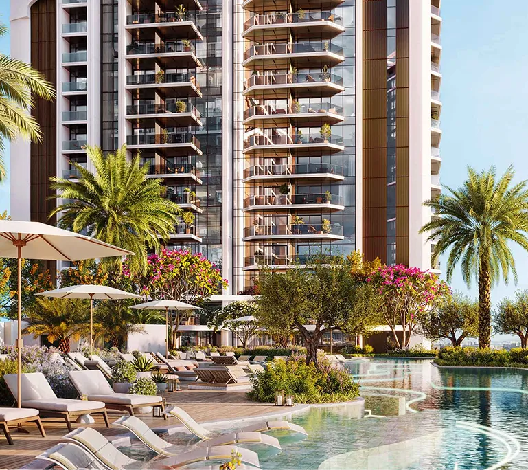 Modern high-rise building with glass balconies overlooking a landscaped pool area with palm trees, lounge chairs, and umbrellas.