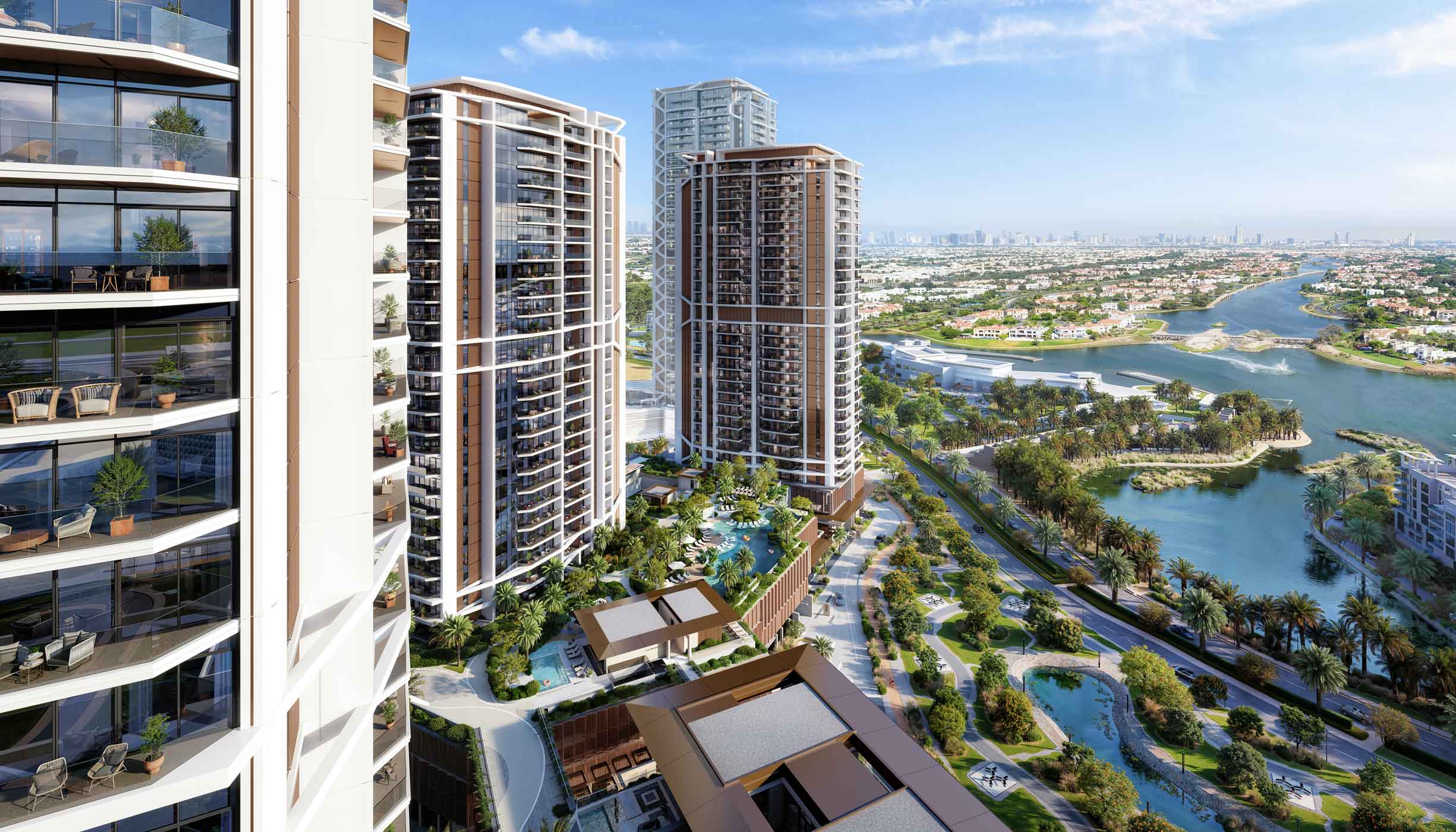 Aerial view of modern high-rise residential buildings with balconies overlooking landscaped gardens, swimming pools, and waterways under a clear blue sky.