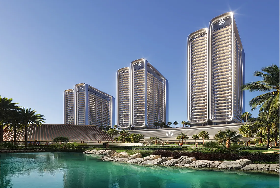 Four tall modern residential buildings with illuminated Mercedes-Benz logos, surrounded by palm trees and a turquoise water body under a clear sky.