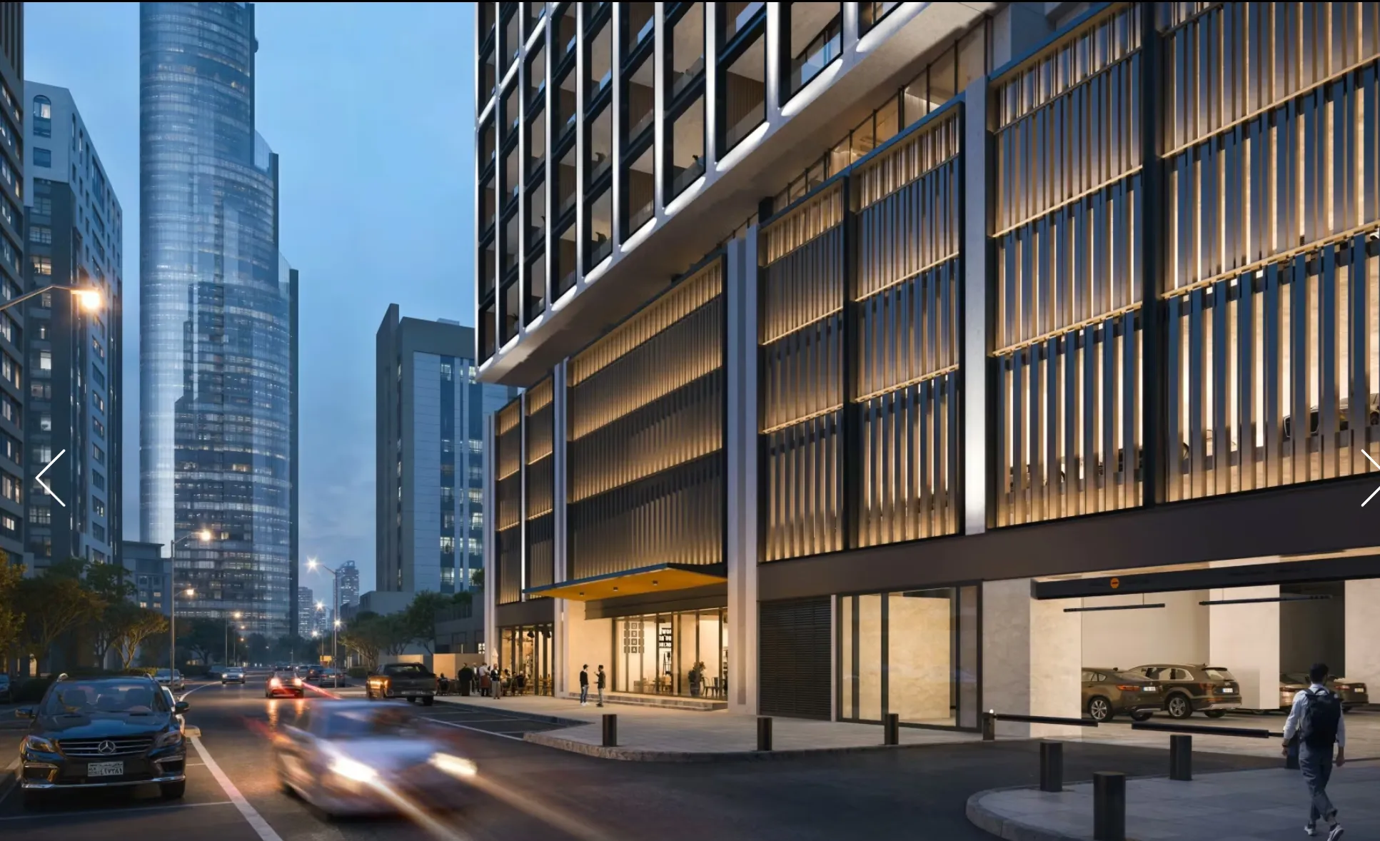Modern city street at dusk with tall glass buildings, cars driving by, and a lit high-rise building with vertical light panels.