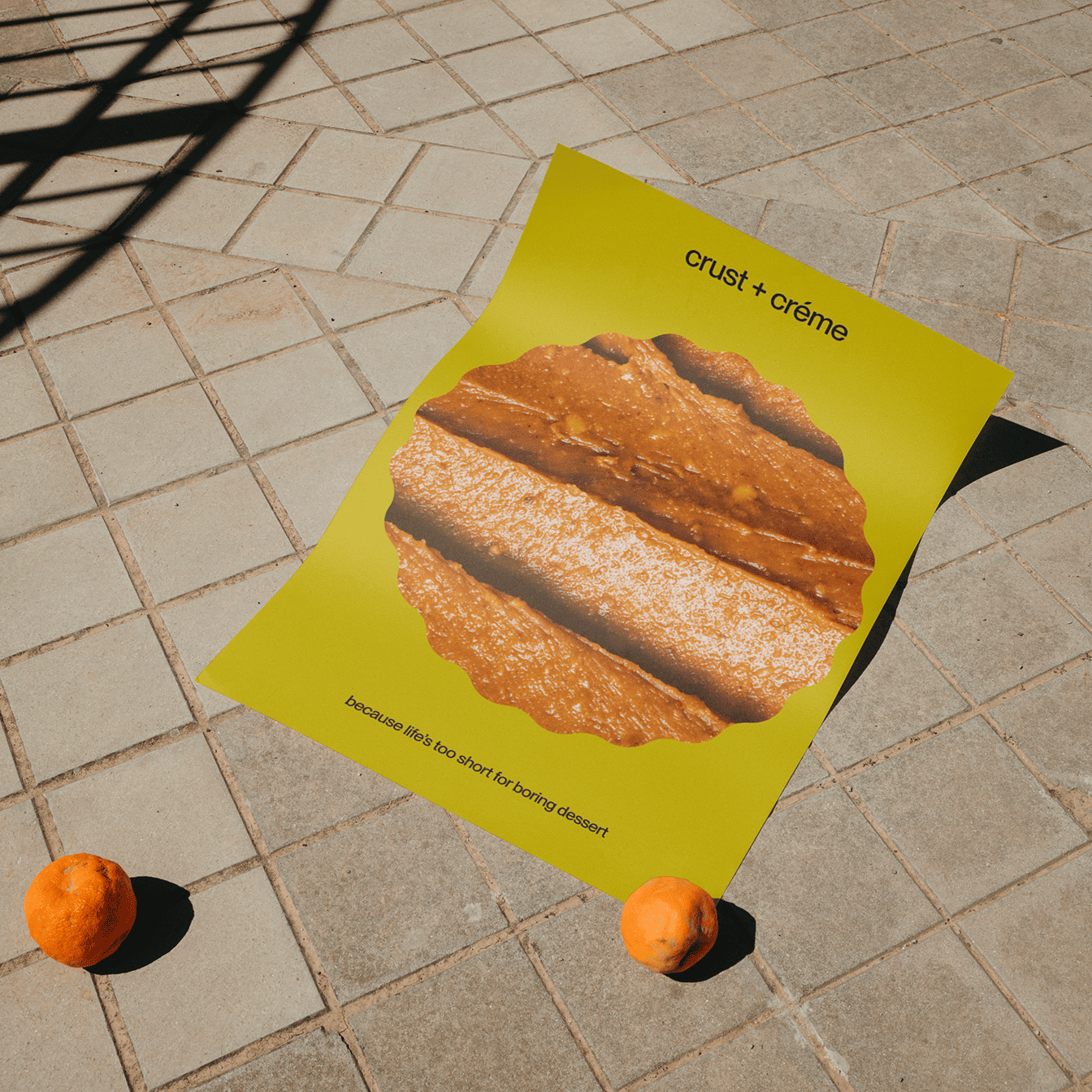 Poster on tiled ground with image of dessert crust and text reading 'crust + crème' and 'because life’s too short for boring dessert', flanked by two oranges.