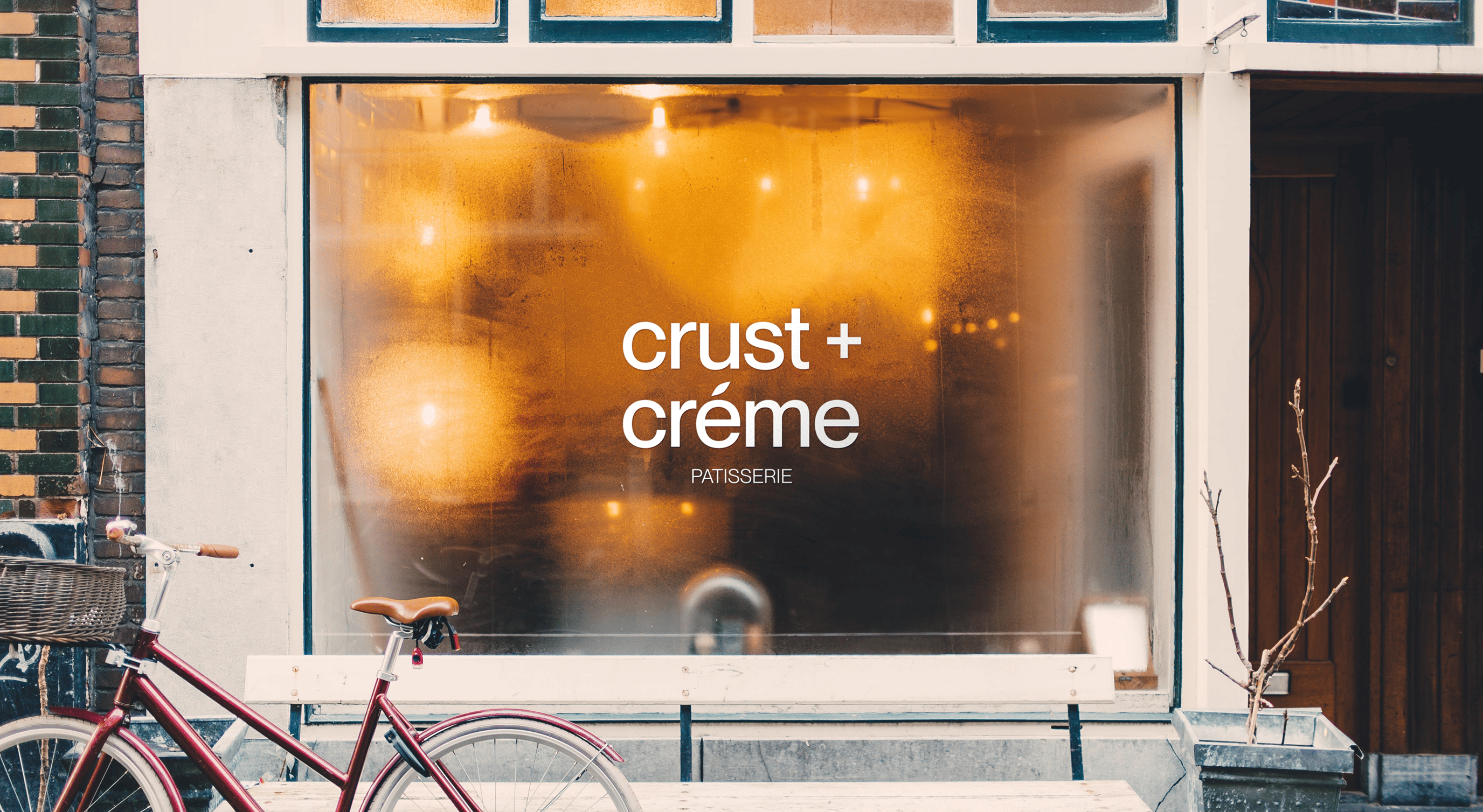 Frosted window of a patisserie with the sign 'crust + crème' and a red bicycle with a basket parked in front.