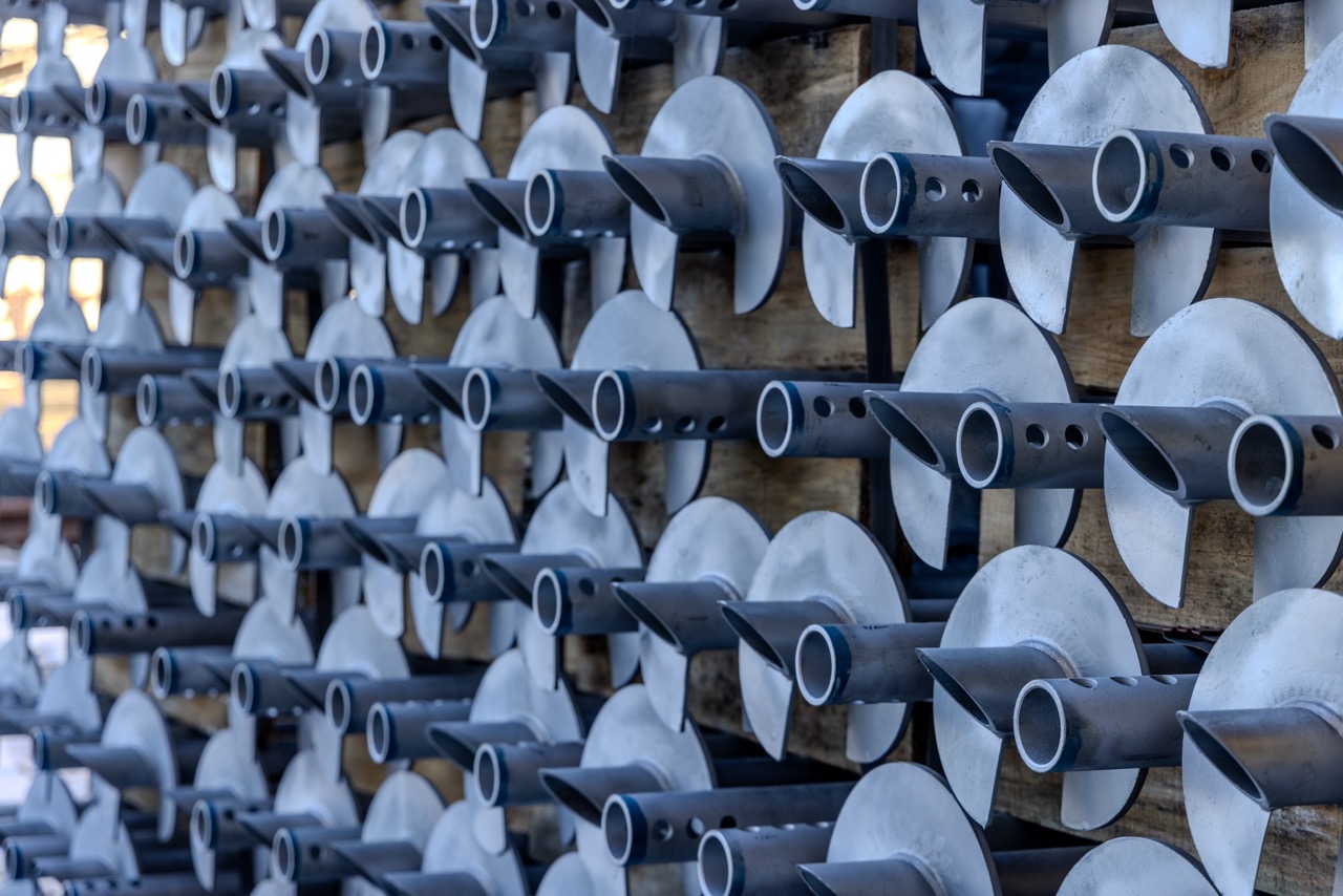 Rows of finished galvanized steel screw piles stacked horizontally on wooden pallets.