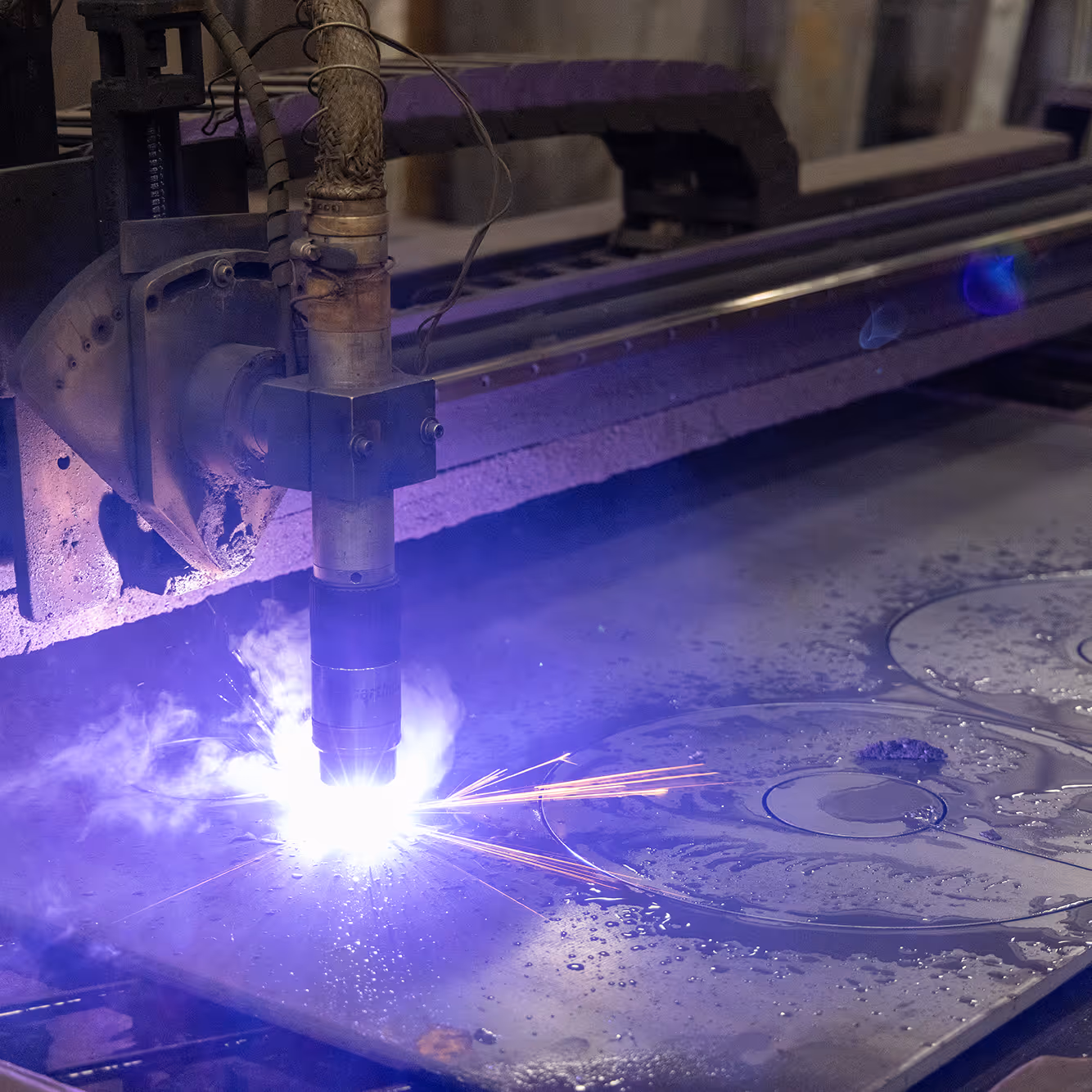 Industrial plasma cutting machine emitting bright blue sparks while cutting metal sheets.