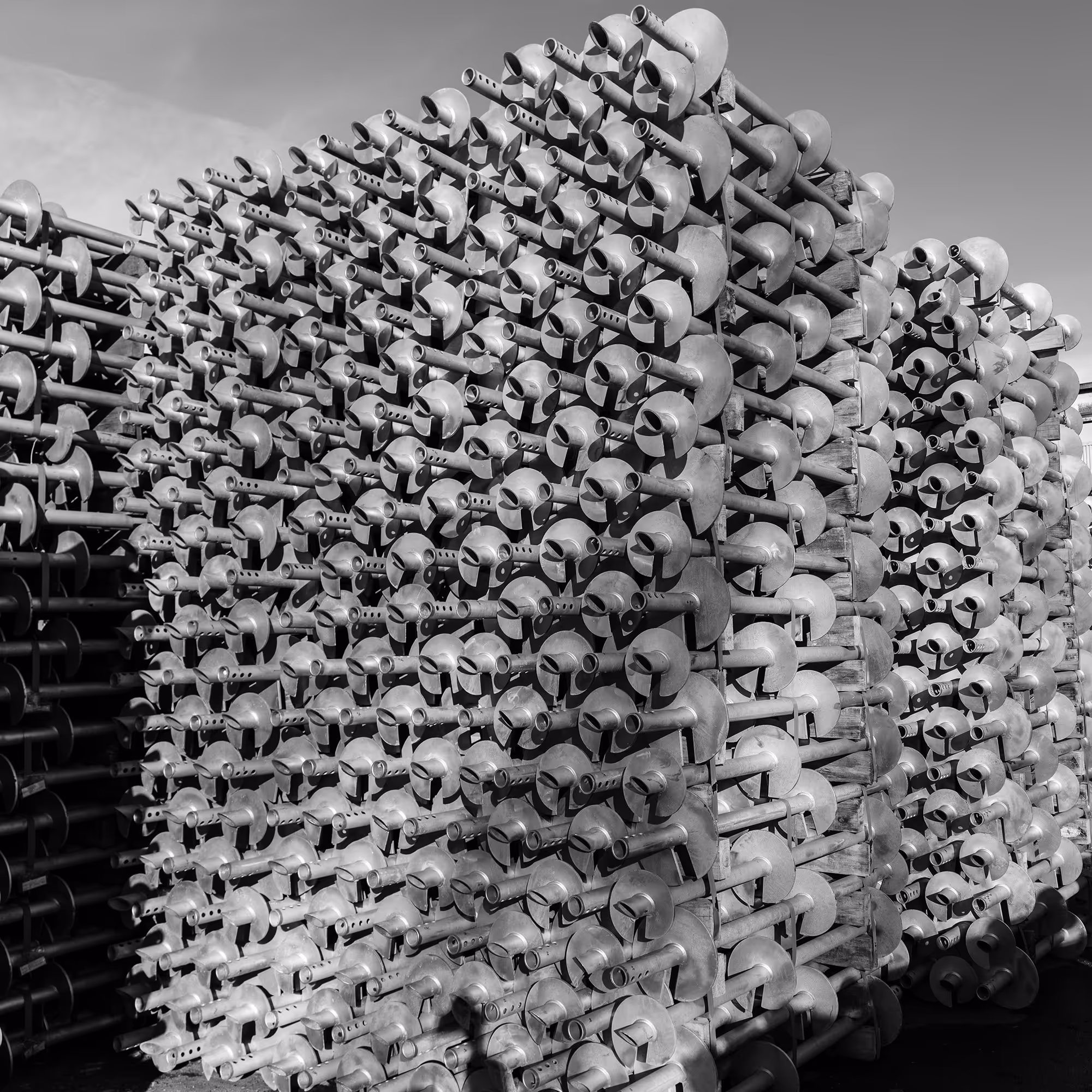 Large stack of metal screw pile foundations arranged outdoors under a clear sky.