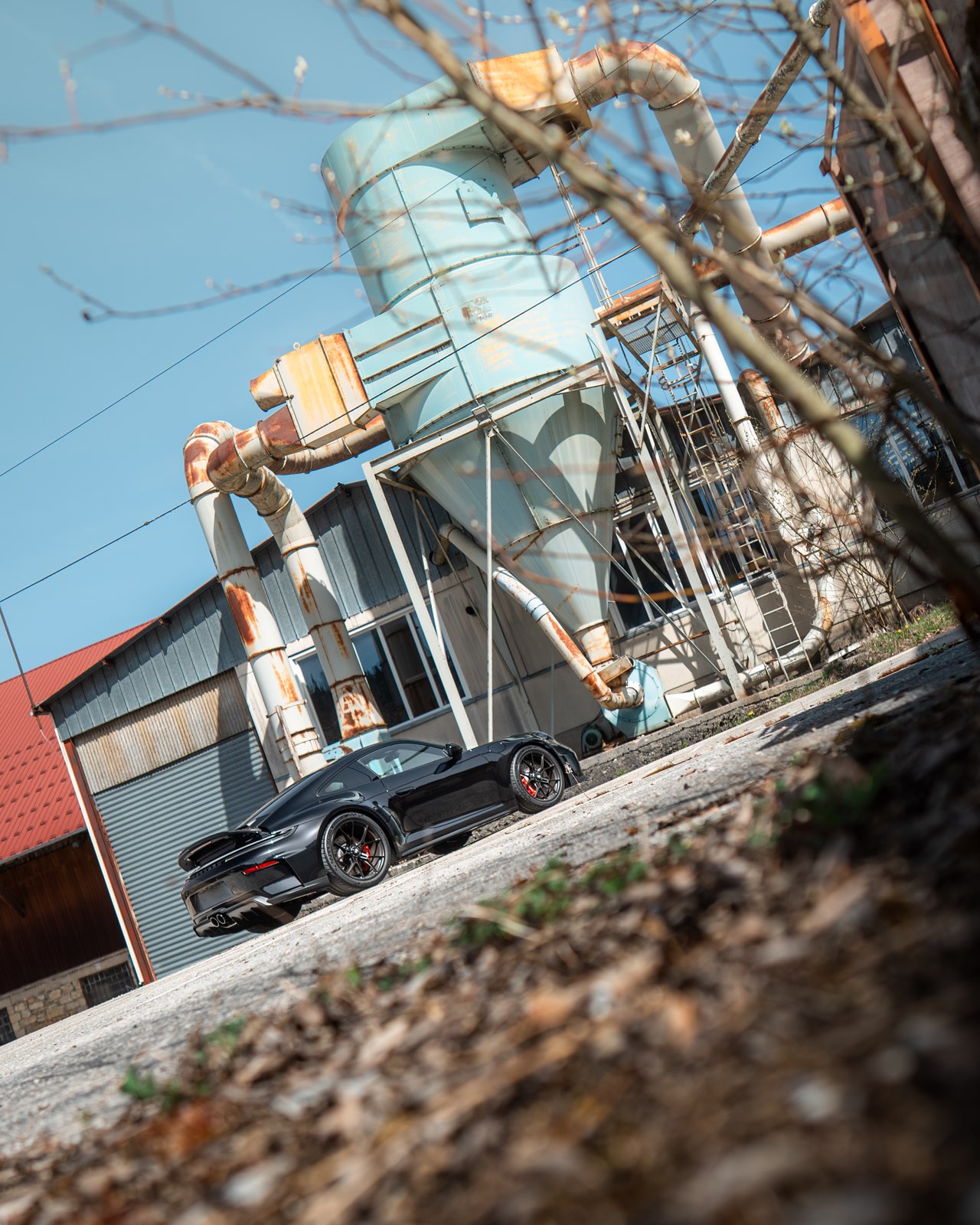 Porsche 911 GT3 noire de trois quarts arrière, devant un bâtiment industriel