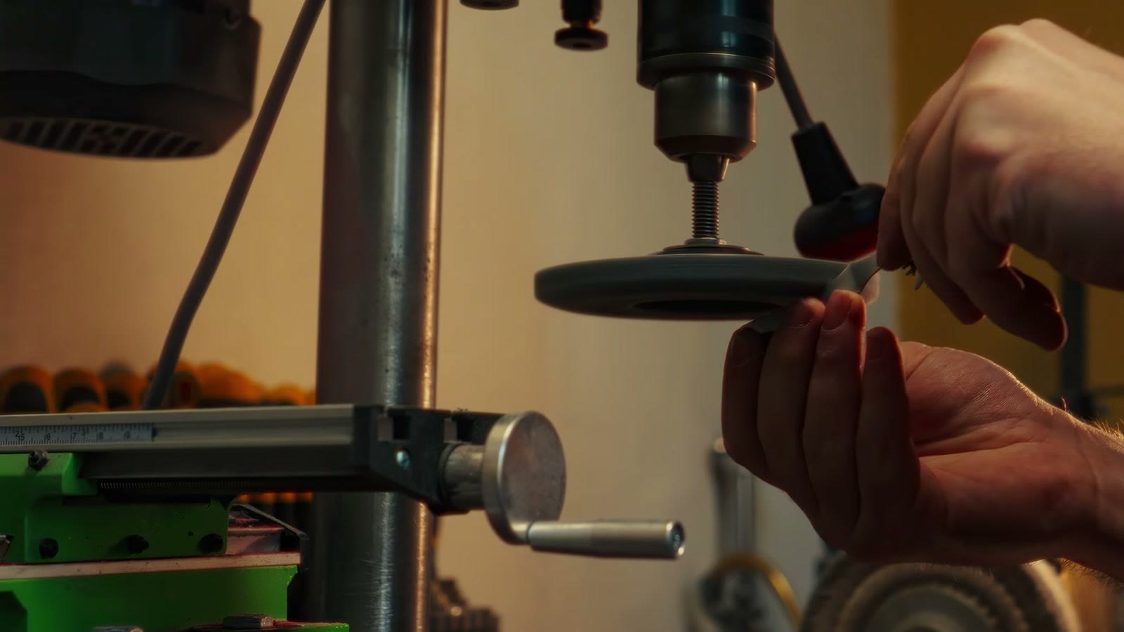 Des mains à la perceuse à colonne, dans un atelier