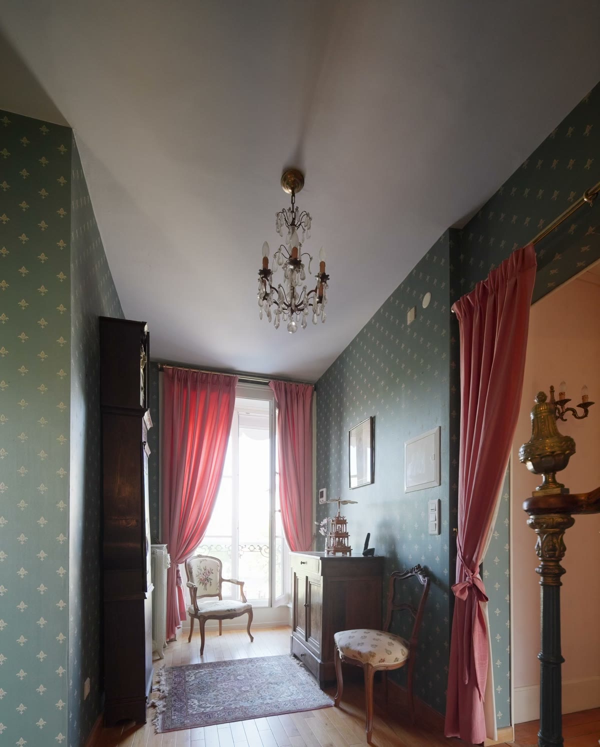 Une chambre aux murs verts, parquet et lustre d’époque