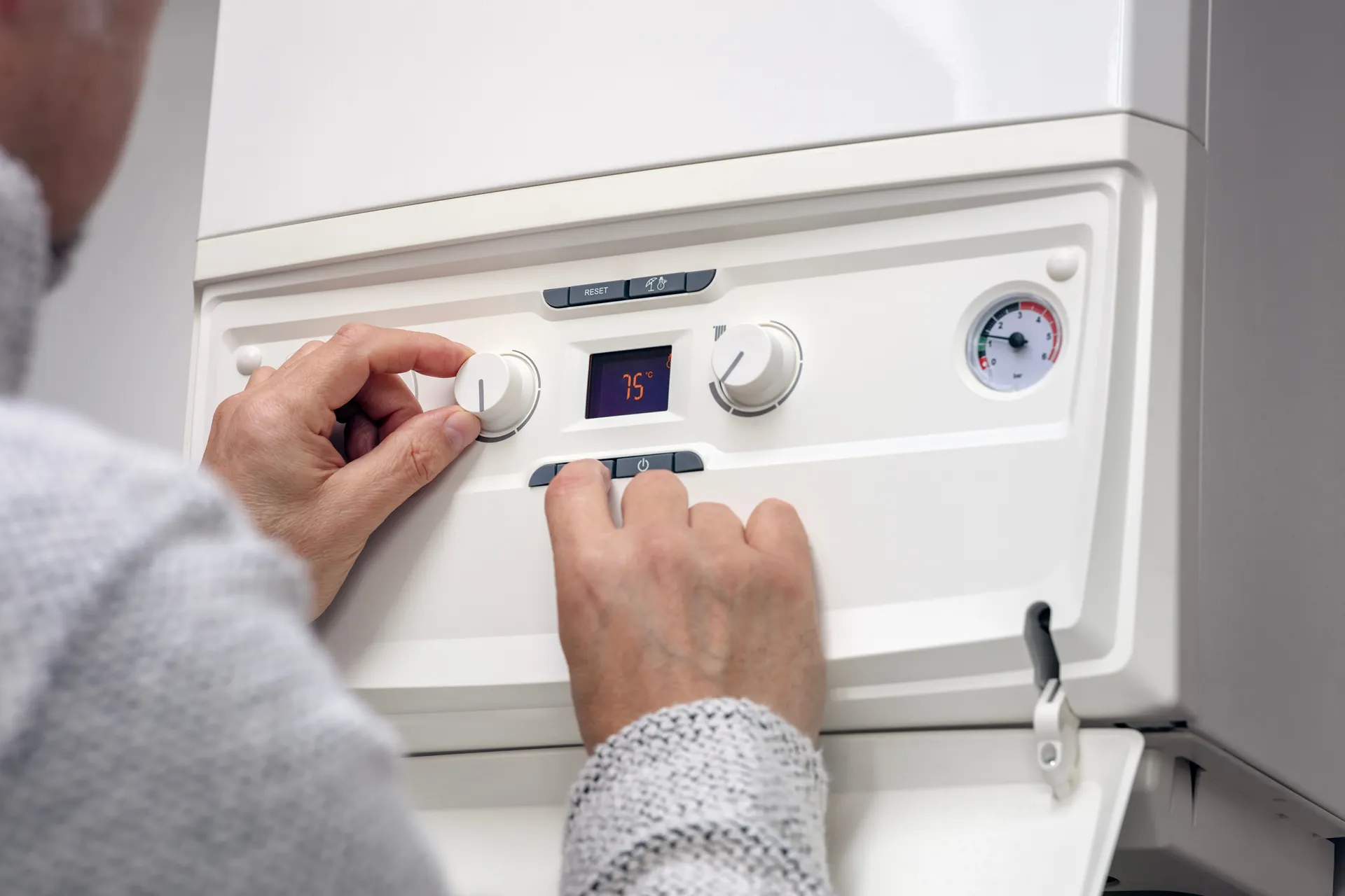 Person adjusting temperature dial on a white boiler control panel showing 75°C.
