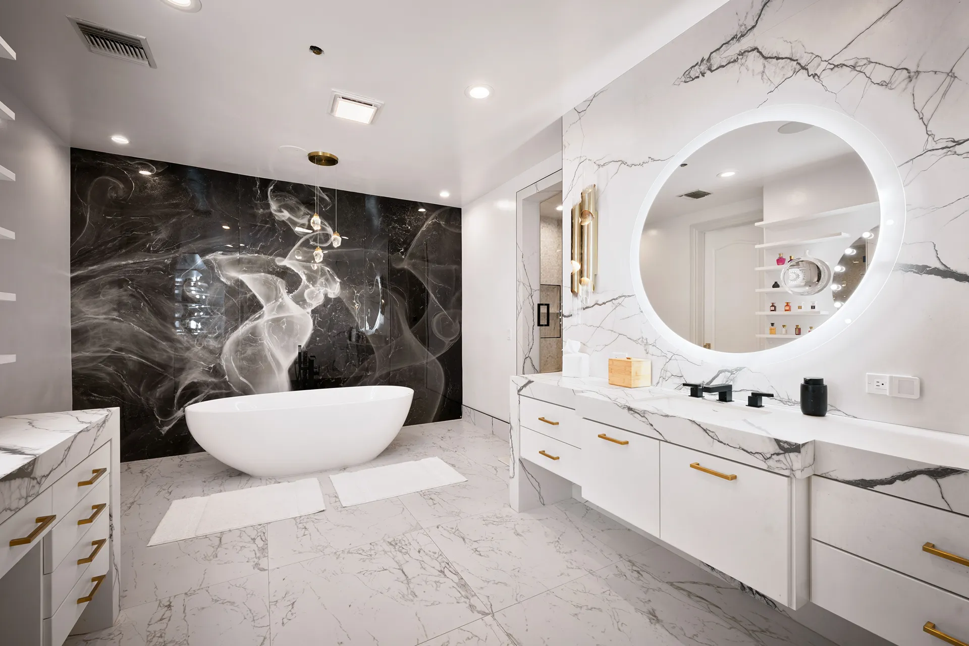Modern bathroom with white freestanding bathtub, dark artistic wall, marble floor and countertop, and round illuminated mirror.