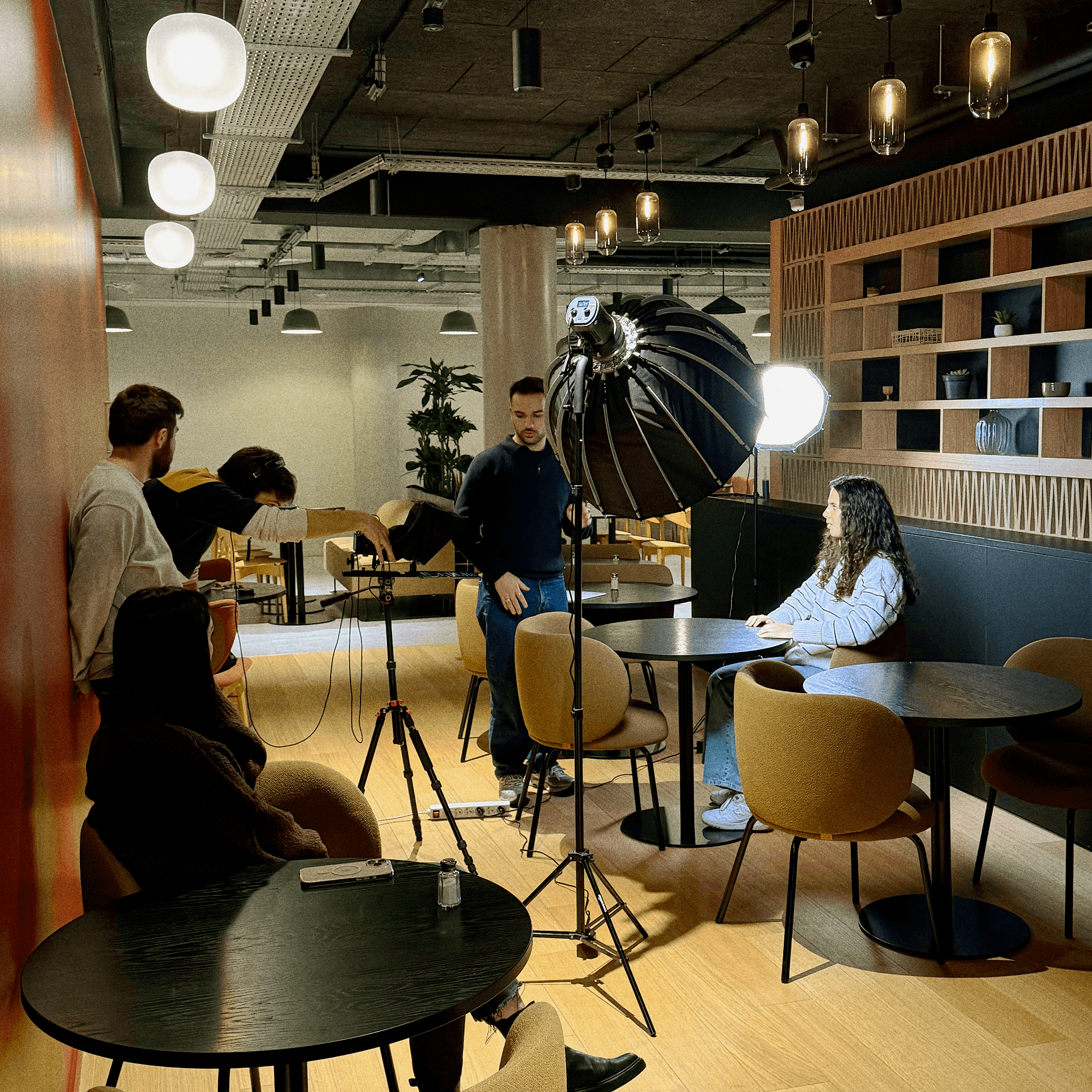 Une séance photo en intérieur avec une femme assise tenant une pose, entourée de quatre personnes réglant l'éclairage et le matériel dans un décor moderne.