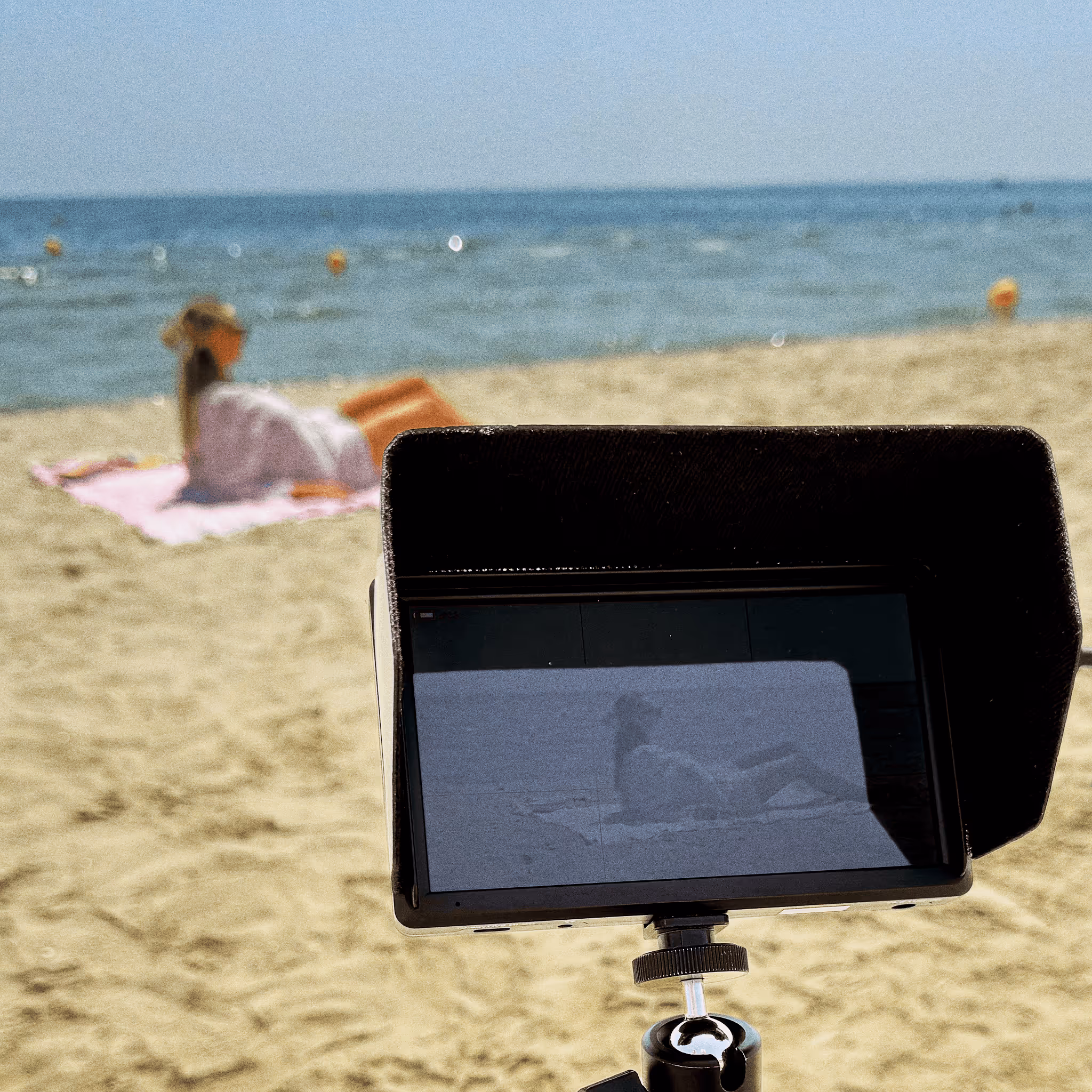Femme allongée sur une serviette rose à la plage, vue à travers l'écran d'une caméra.