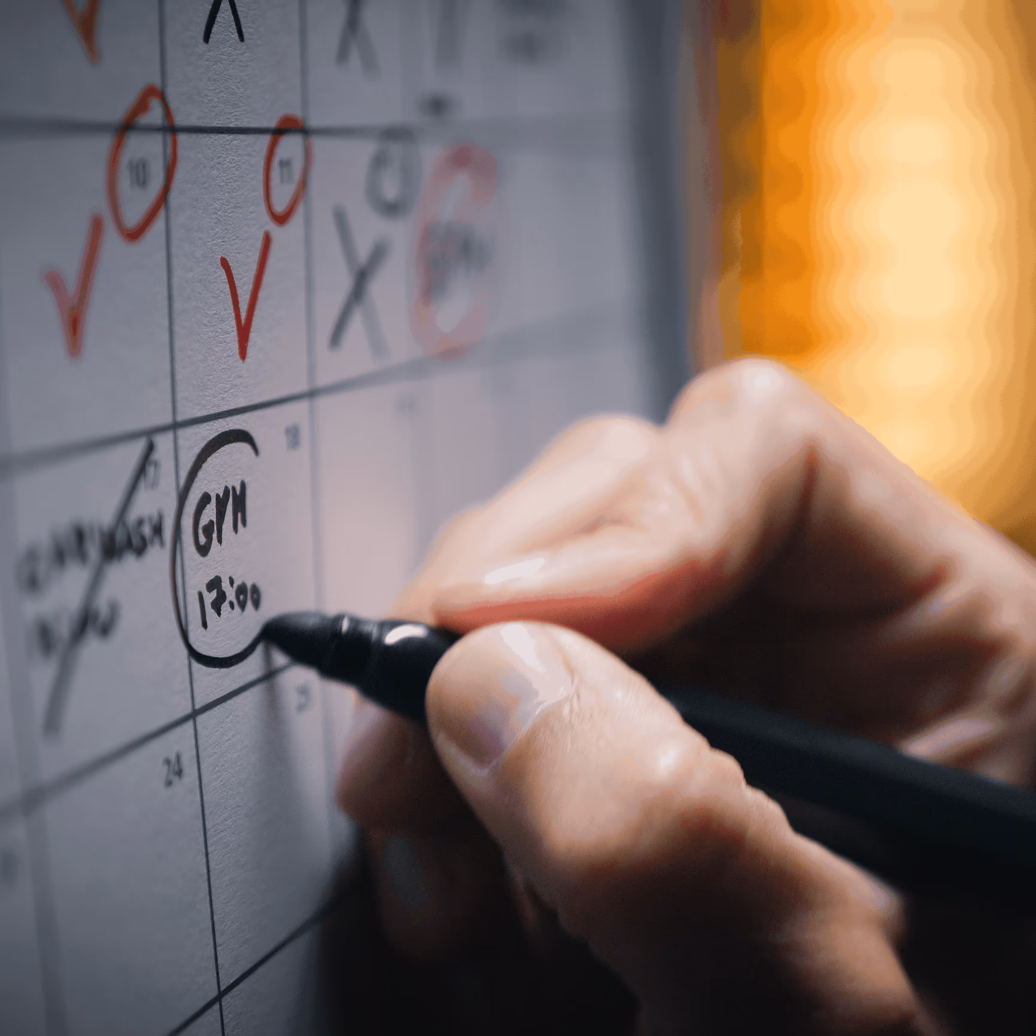 Main écrivant avec un marqueur sur un calendrier, entourant la note 'GYM 17:00'.