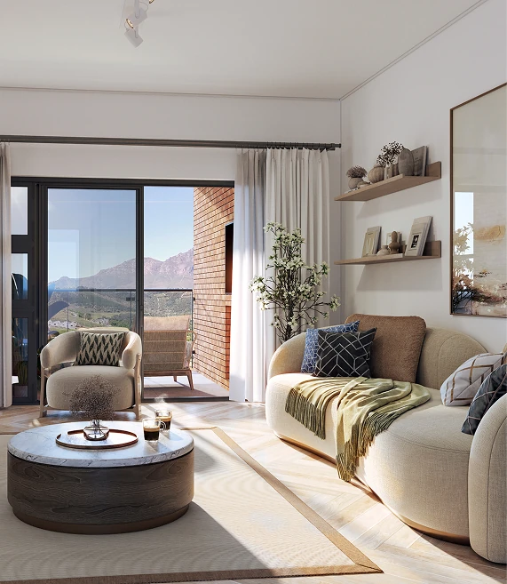 Bright living room with beige curved sofa, green throw, patterned cushions, round wooden coffee table, armchair, and balcony with mountain view.