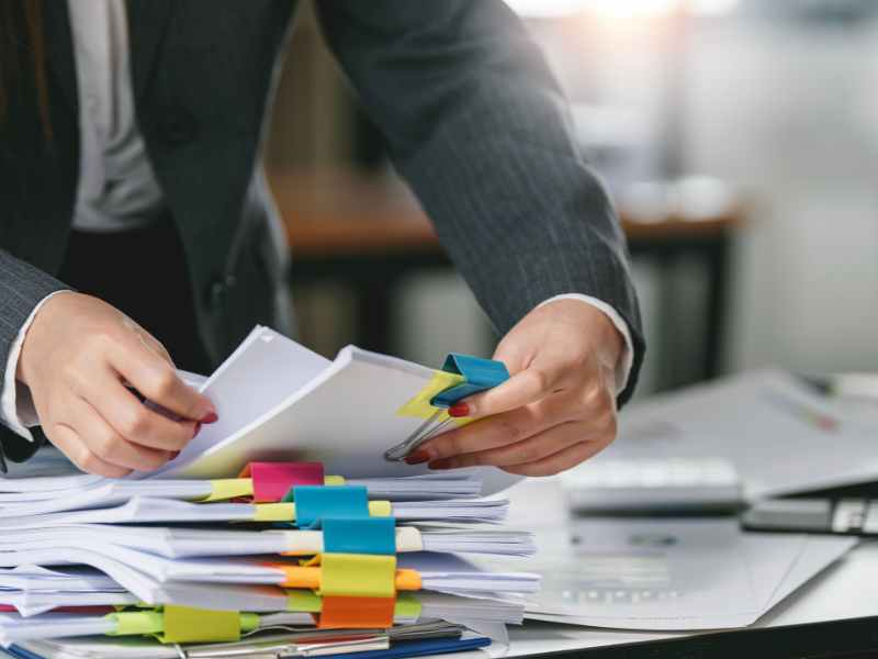 Property manager reviewing stacks of paper insurance certificates during manual vendor compliance tracking