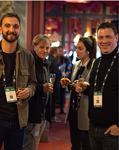 Four people standing together at an event, holding drinks and wearing lanyards, smiling and talking.
