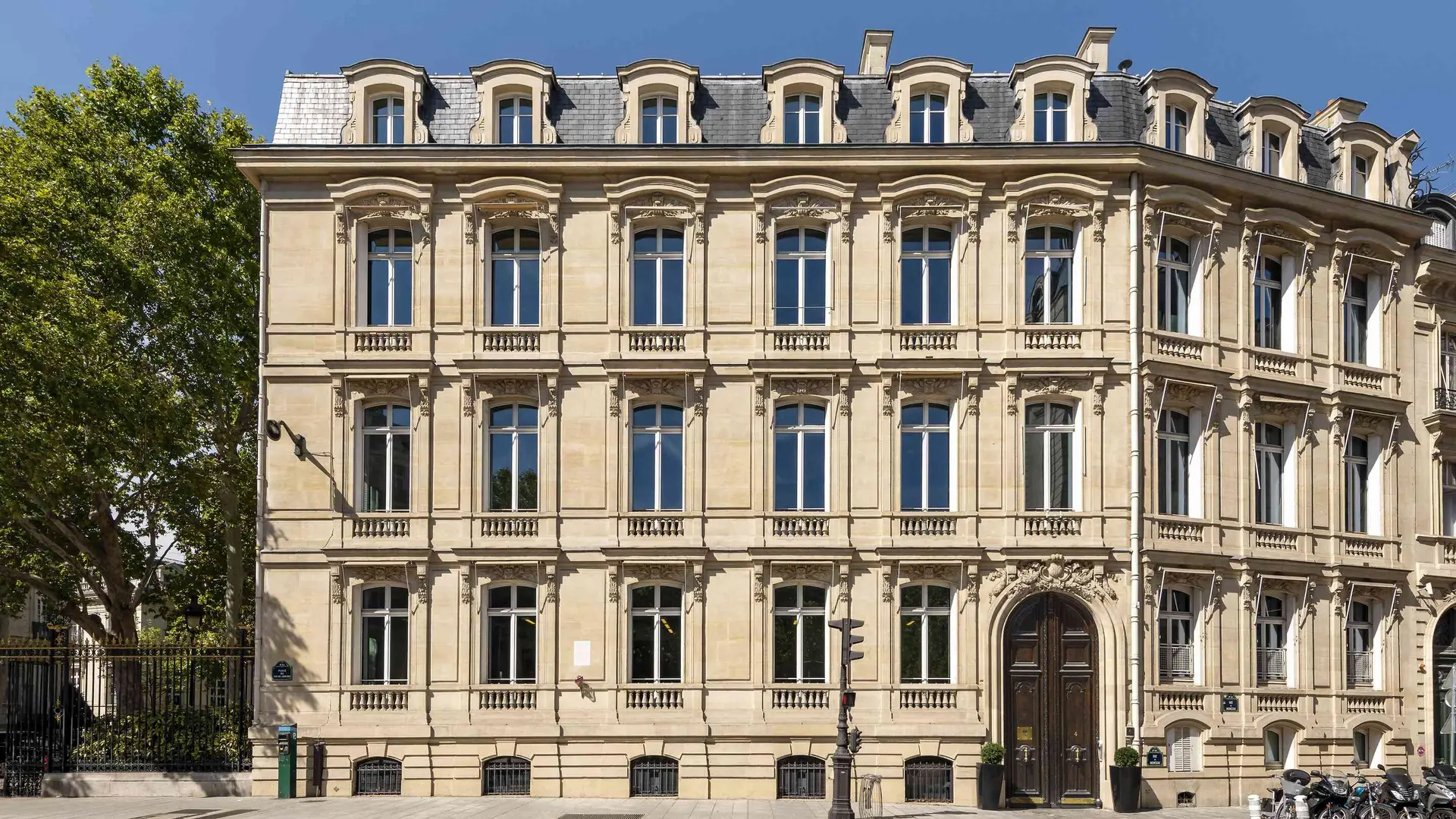 Large beige building with multiple rows of windows and an arched wooden doorway on the ground floor.