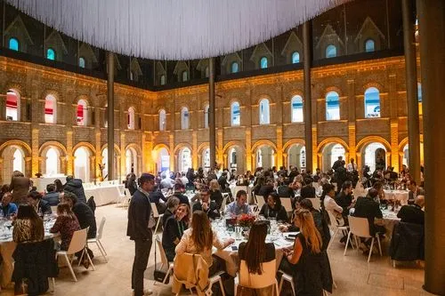 People sitting at tables, dining together in a spacious, well-lit hall with high ceilings and arches.