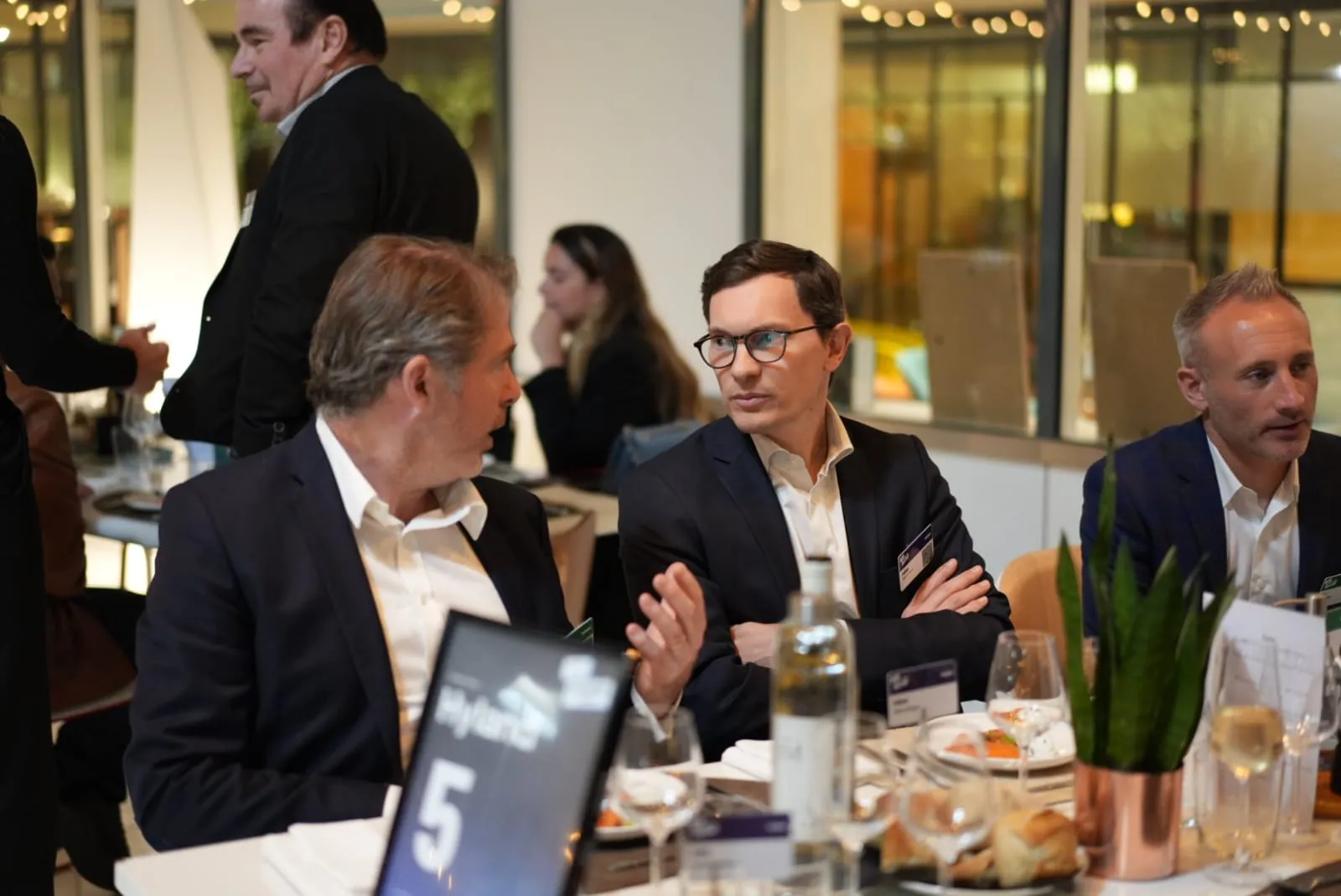 Three men in business attire sit at a table, engaged in conversation during a formal event.