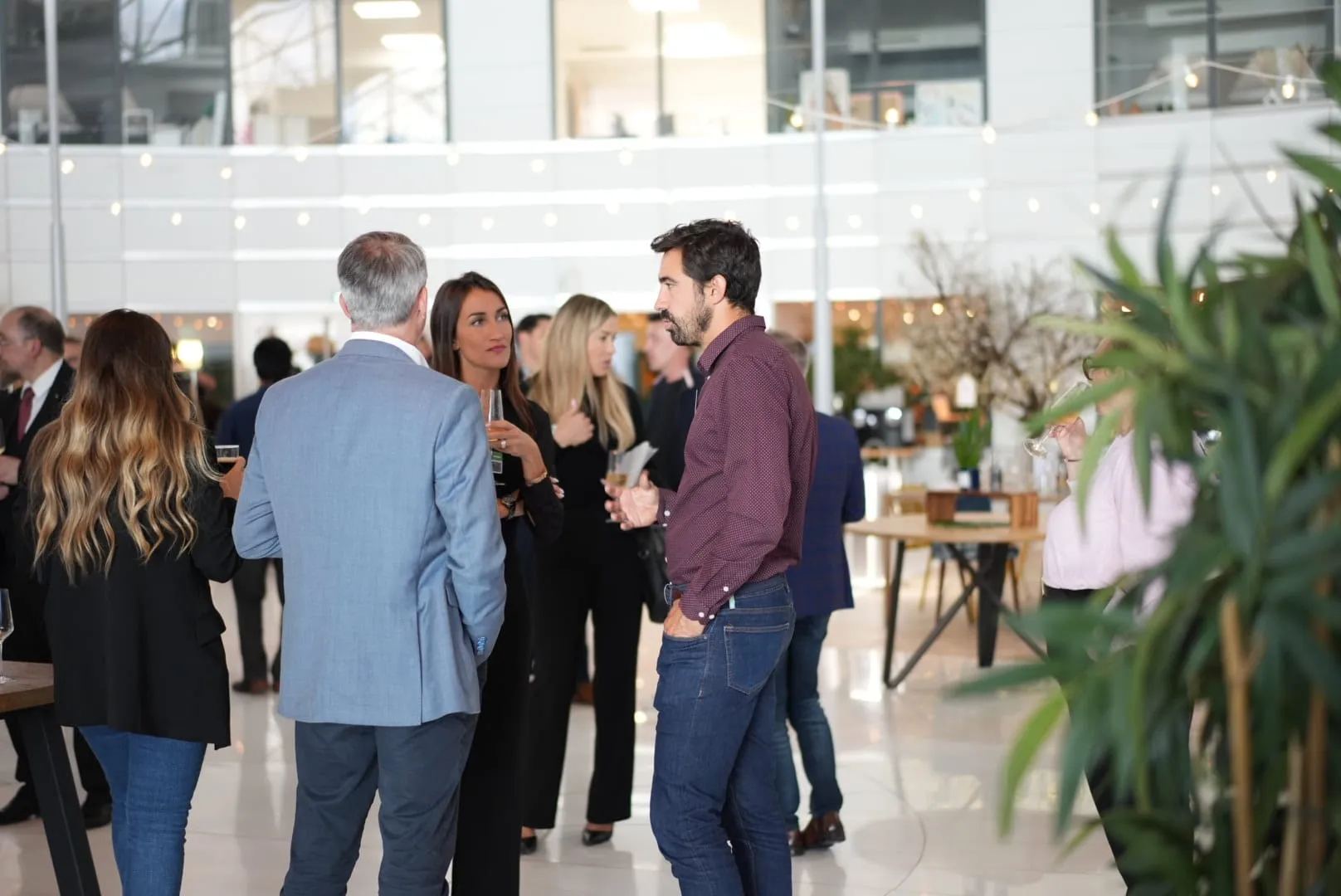 People standing and talking at a social gathering in a bright indoor space.