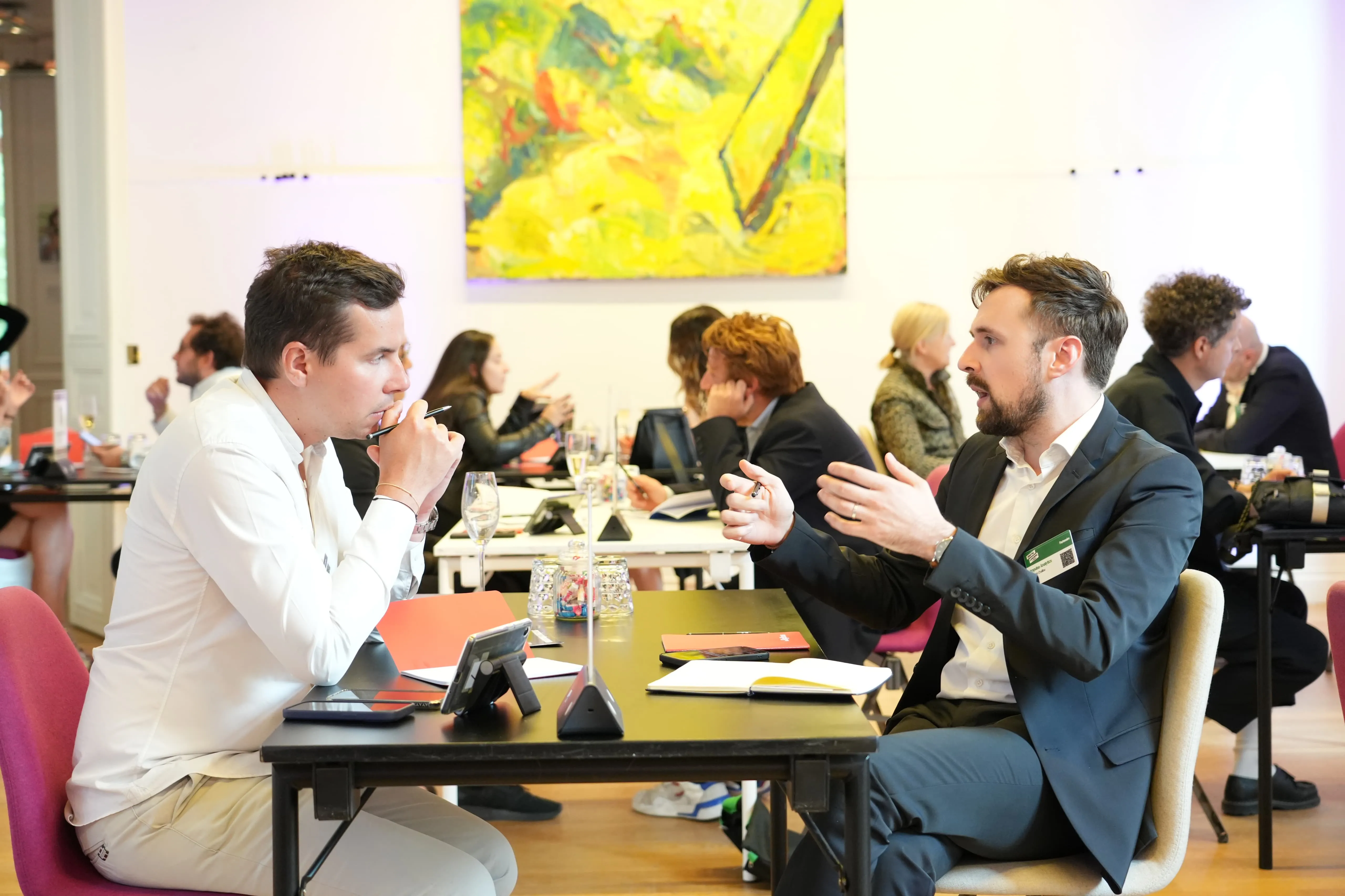 Two men sitting and conversing at a conference table in an indoor setting.