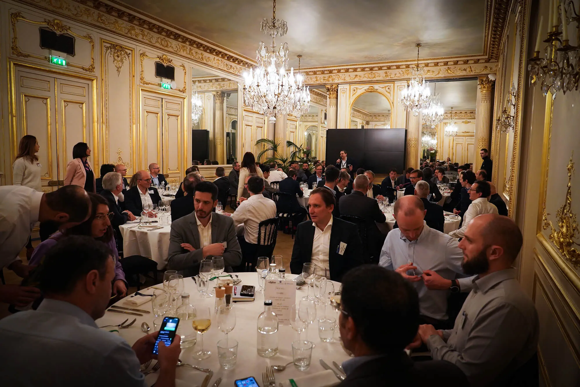 A group of people in formal attire sitting at tables in an elegant dining room.
