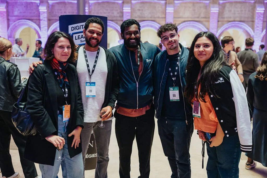 Five people are standing together, smiling, and holding drinks at an indoor event.