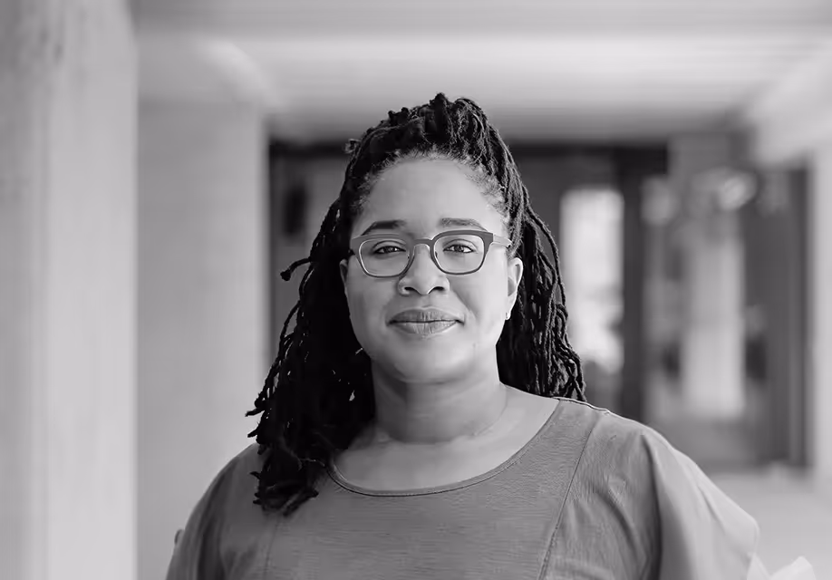 Black and white portrait of Jasmine McNealy standing in a hallway. Her work focuses on data governance and public facing policy research.