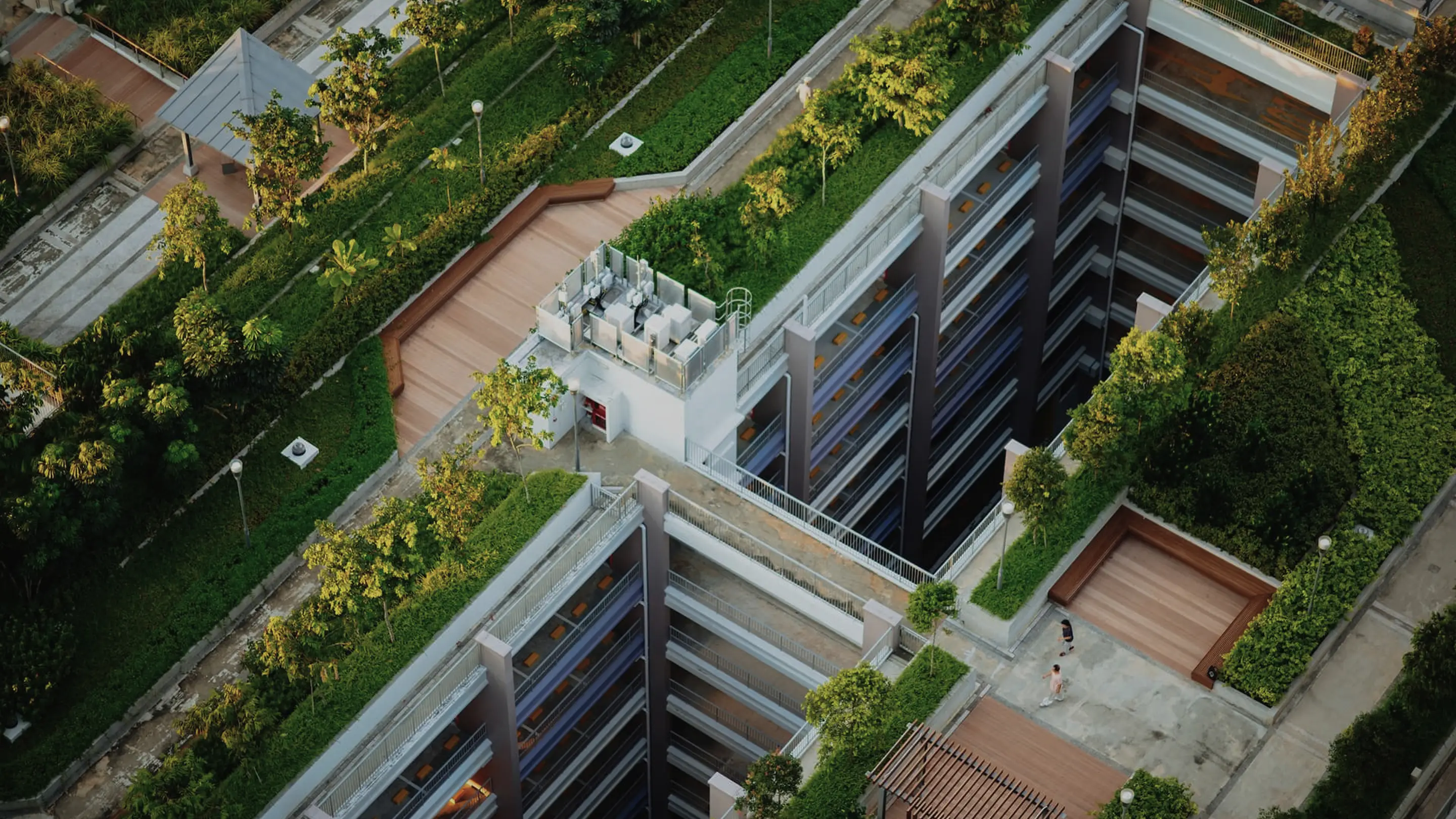 Veduta aerea di un edificio moderno con balconi interni, circondato da aree verdi e vialetti con due persone che camminano.