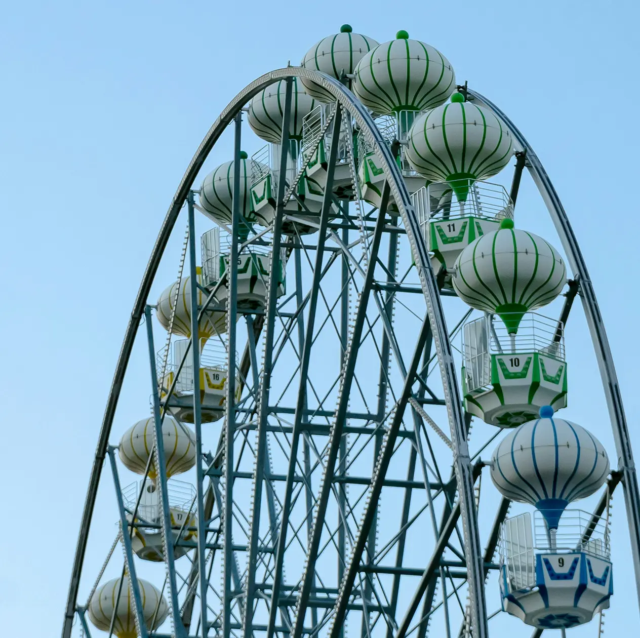 Ferris wheel with gondolas shaped like hot air balloons in green, yellow, and blue against a clear sky.