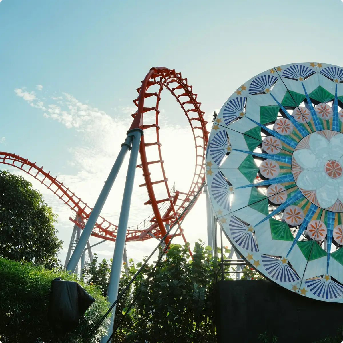 Traccia rossa di montagne russe con un grande disco decorativo colorato in un parco a tema durante il giorno.