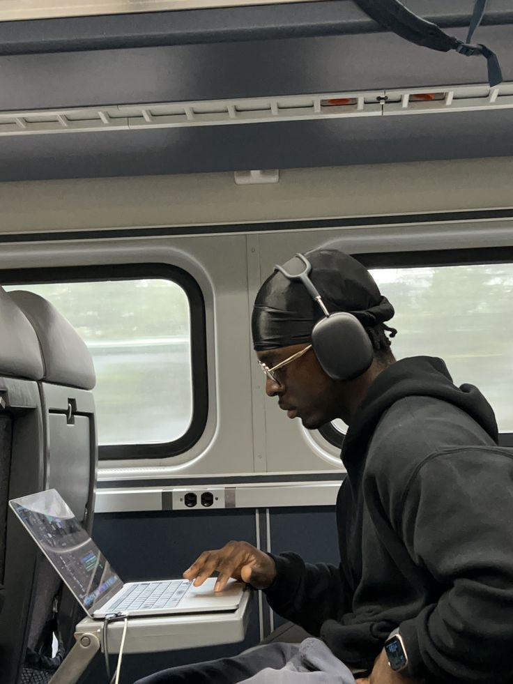 Young man working on a laptop with headphones on, in a train.