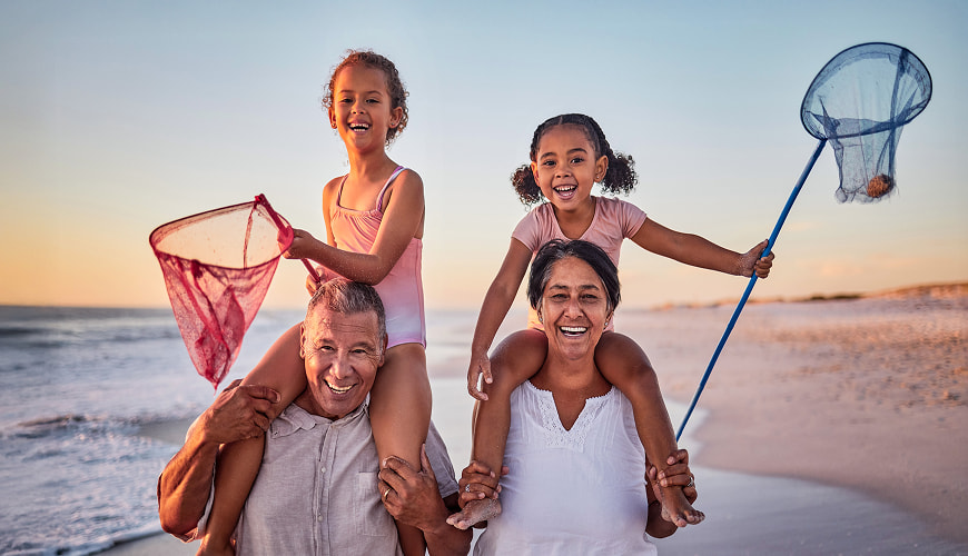 Retired couple walking on the beach with their grandchildren on their shoulders