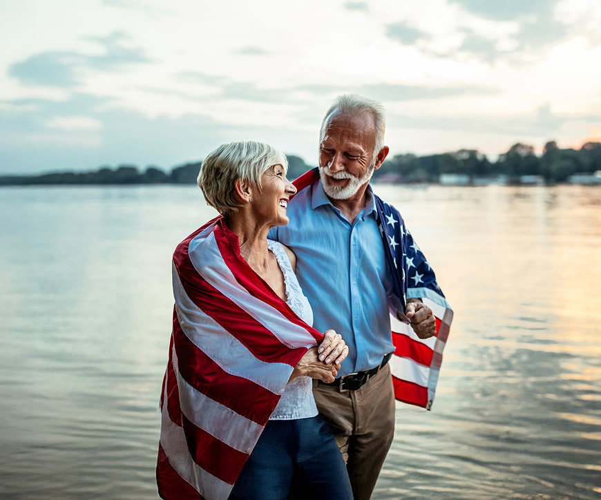 Retired couple walking by a lake wrapped in an American flag