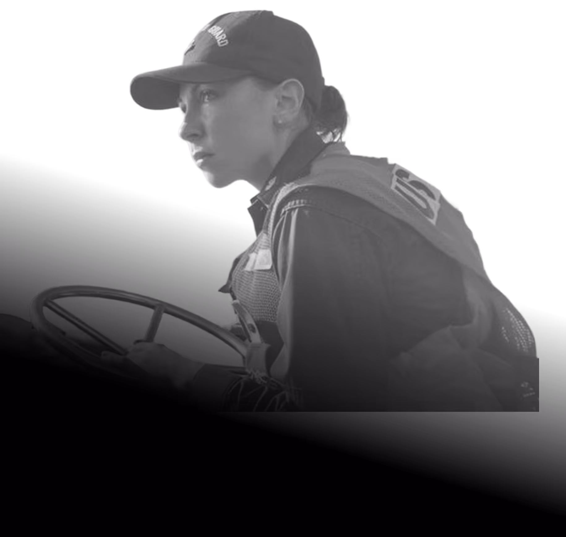 Focused female coast guard in uniform steering a boat wheel.