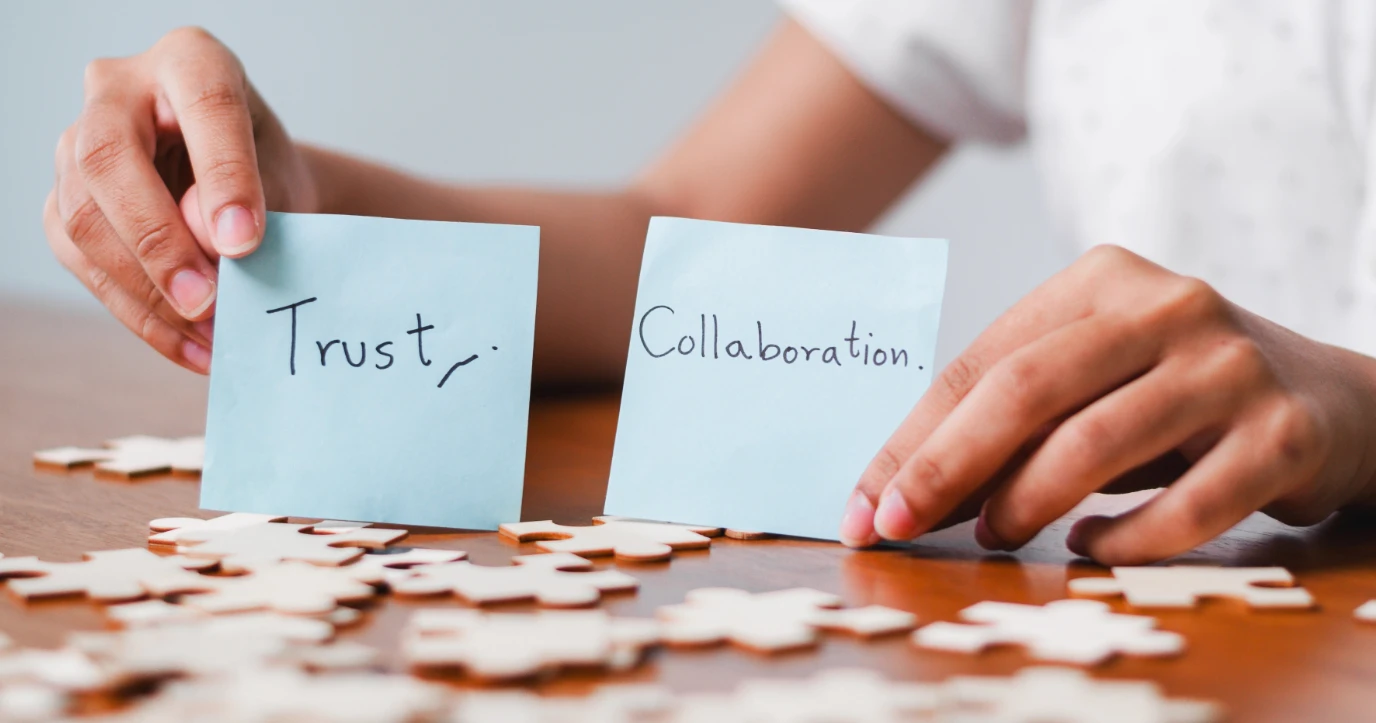 woman's hands holding two handwritten notes; one has the word 'trust', the other has the word 'collaboration'