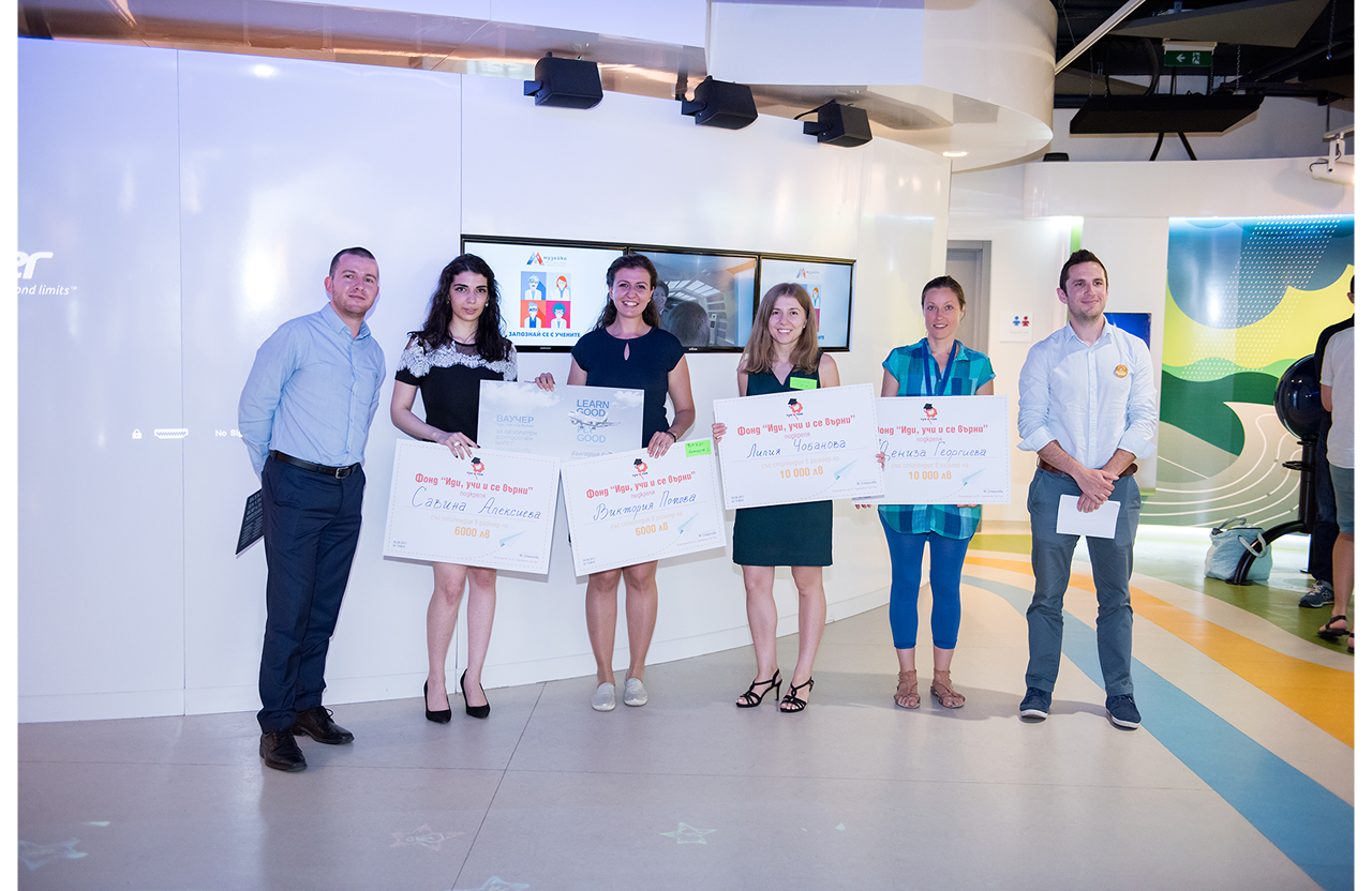 Group of six people standing indoors holding large scholarship checks during an award event.
