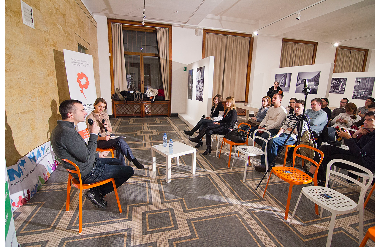 Two people speaking with microphones in a small room audience seated facing them.