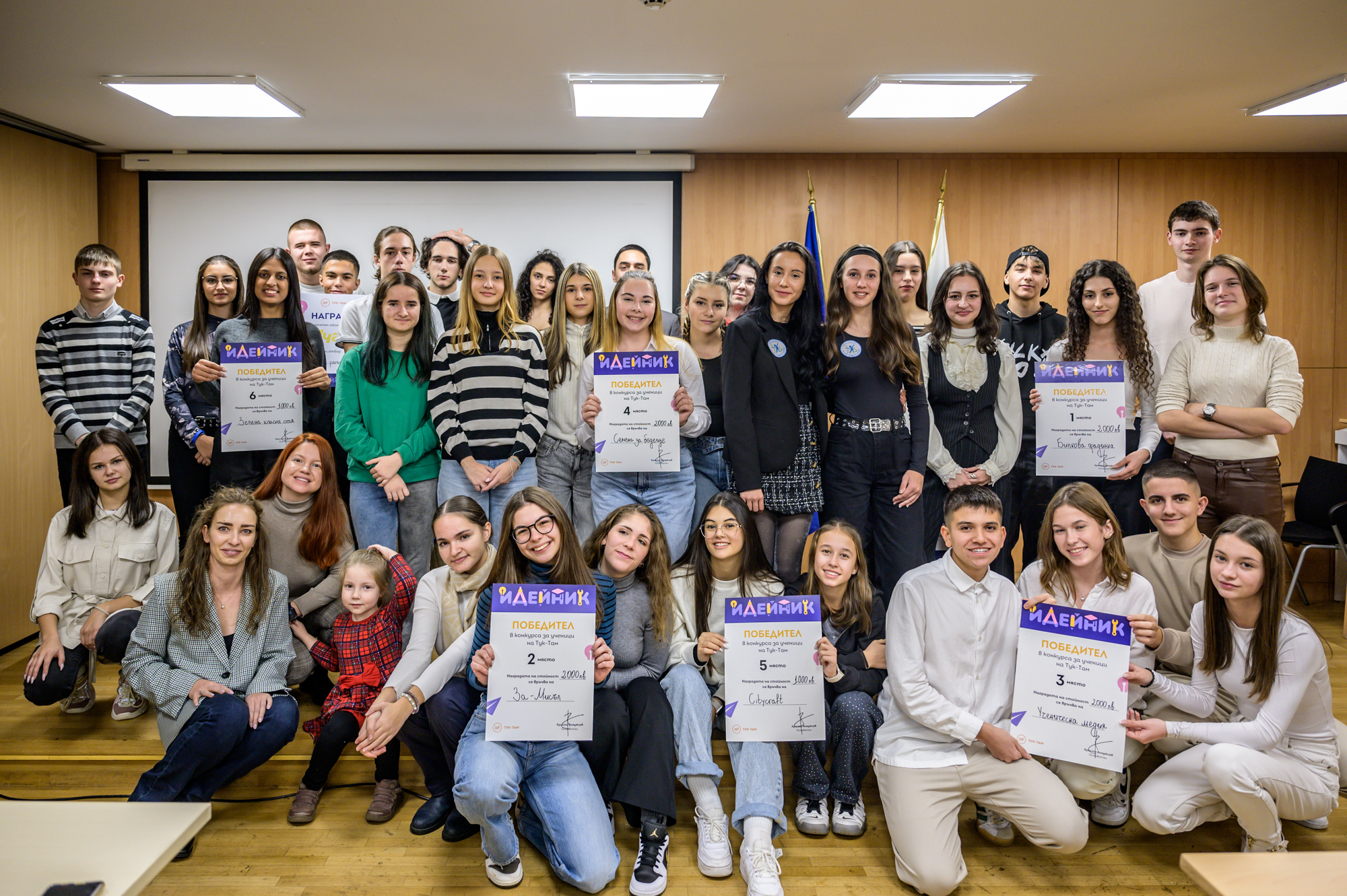 Large group of young people posing indoors, some holding certificates and smiling. Winners from Ideinik 2024