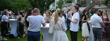 People socializing near tall white cocktail tables at an outdoor garden party.