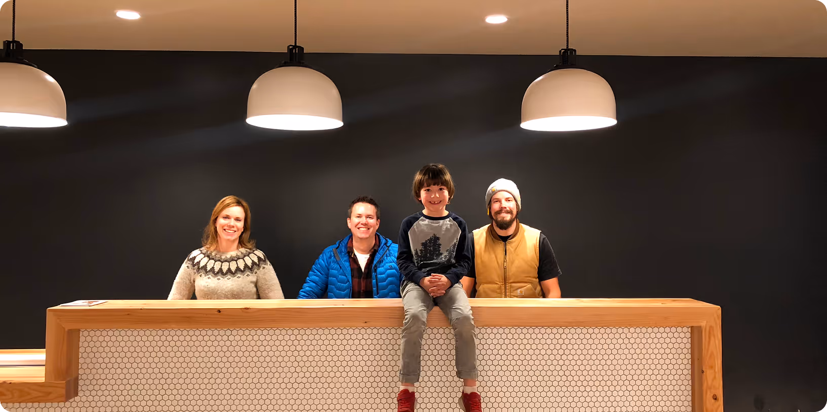 Three adults standing behind a countertop with a child sitting on top of the counter
