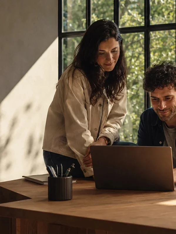 Two colleagues reviewing work on a laptop by a window