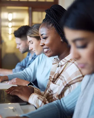 Four diverse people sitting in a row working on laptops and smiling.