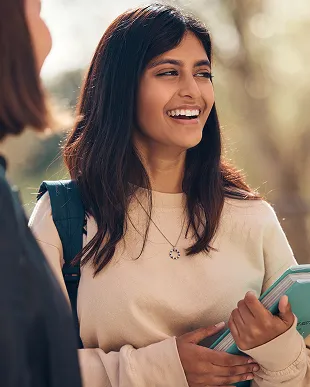 Smiling young woman with long dark hair holding notebooks outdoors.