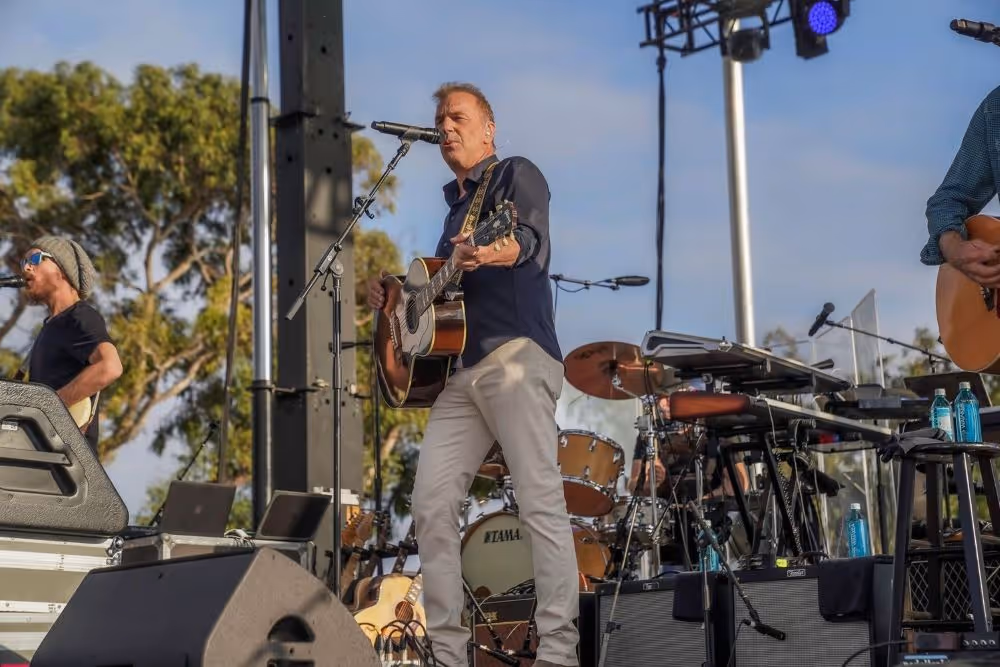 Male singer playing an acoustic guitar and singing on an outdoor stage during a live performance.