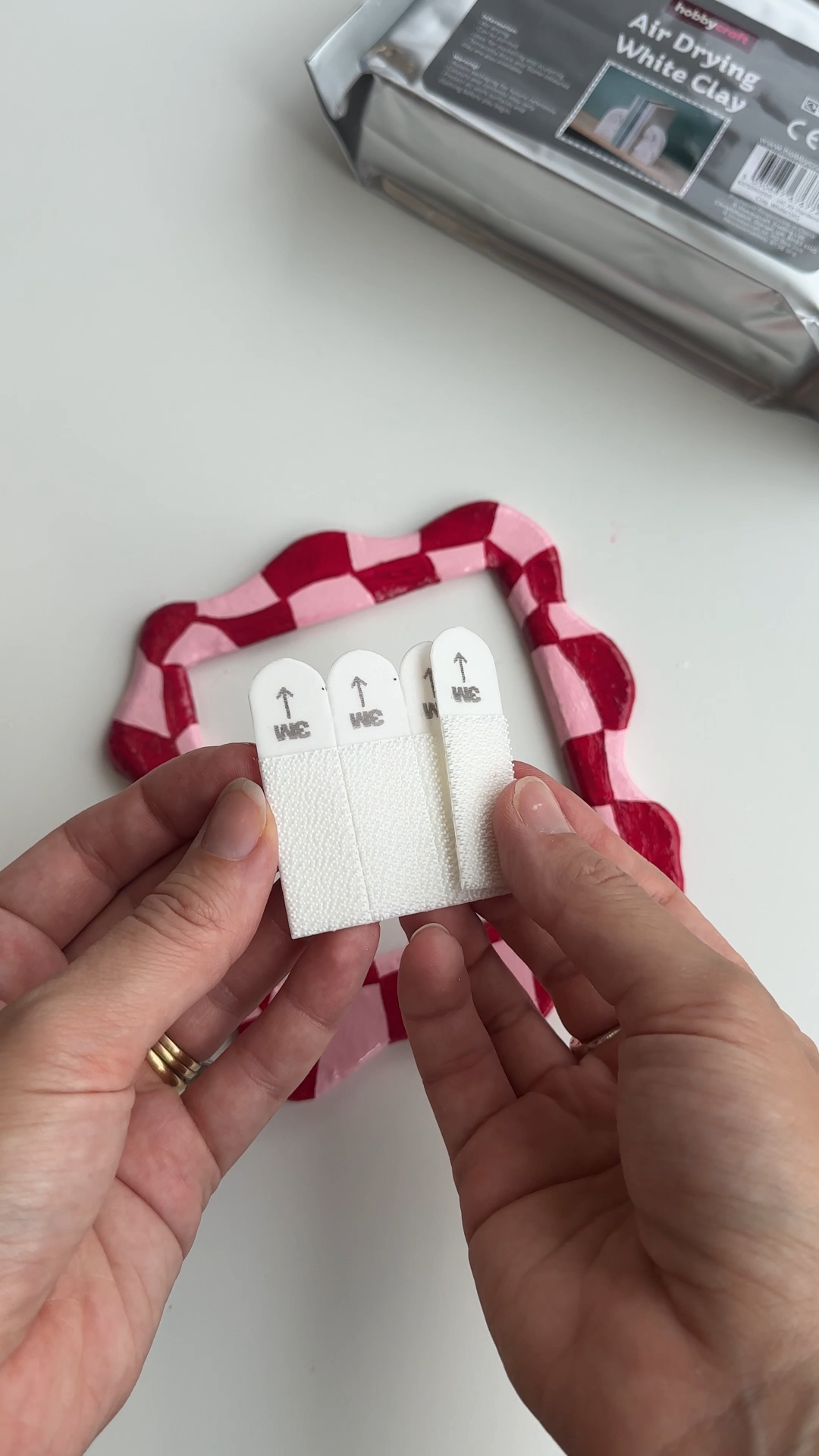 Applying command strips to the back of an air dry clay light switch cover for easy wall mounting.