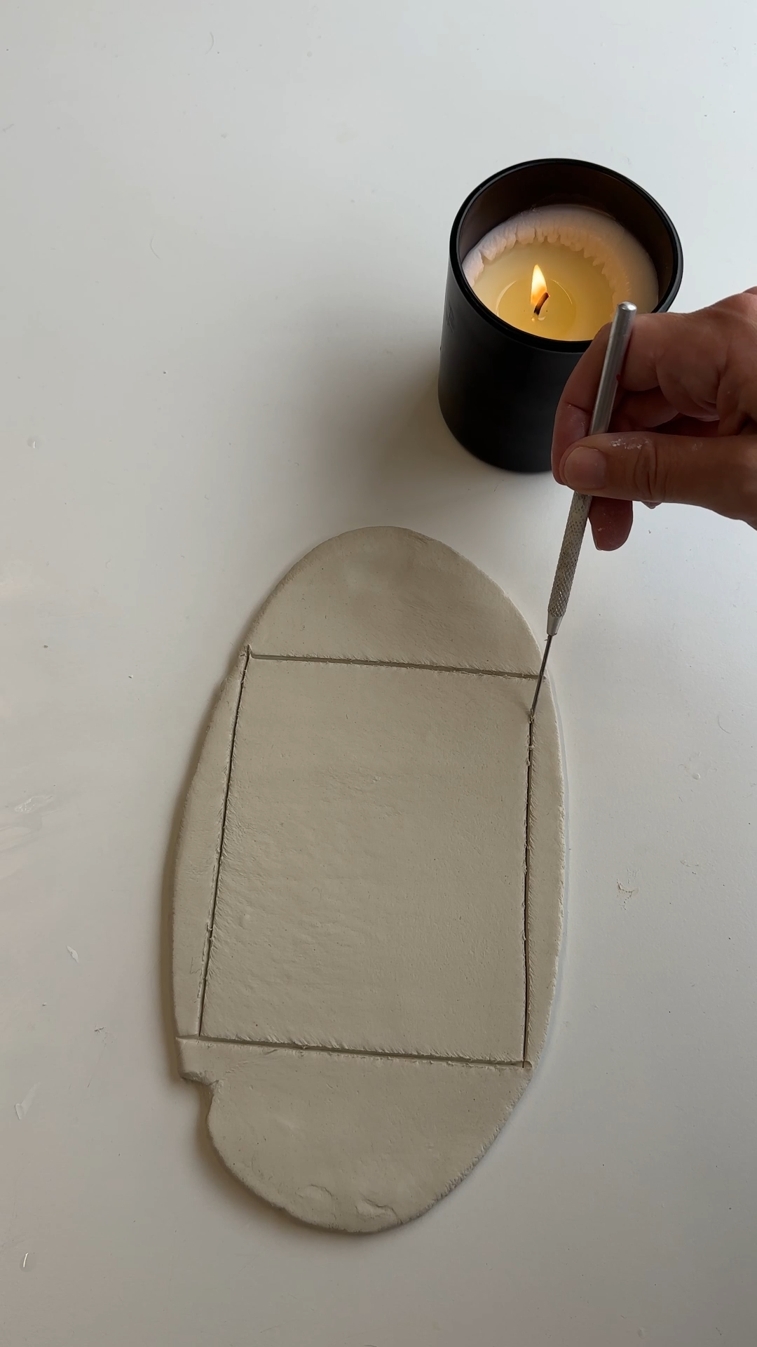 Hand using a craft knife to cut a rectangle from a rolled slab of air dry clay to form the base of a DIY clay notepad.